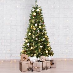 a christmas tree with presents under it in front of a white brick wall and lights