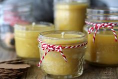 three jars filled with yellow candles on top of a wooden table next to cookies and candy canes