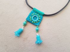 a crocheted square with tassels and beads hanging from a leather cord