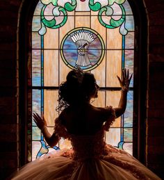 a woman standing in front of a stained glass window with her hands up to the side