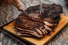 a person cutting up some meat on top of a wooden board with a knife in it