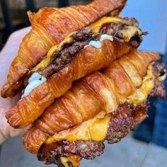 a croissant sandwich with meat and cheese on it being held in someone's hand