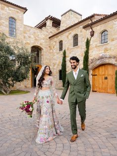 a bride and groom walking in front of a large stone building holding hands with each other