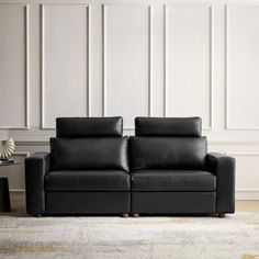 a black leather couch sitting on top of a rug in front of a white wall