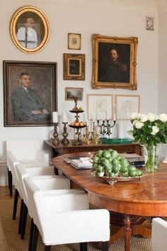 a dining room table with white chairs and pictures on the wall above it, along with flowers in vases