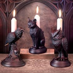 three candles are sitting on a table with two cats and an owl figurine