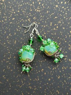 Hand made funky rounded square earrings in vivid green apple colour, wire-wrapped and embroidered with small beads, with dangling green beads. Size: length ca 4cm (without hooks), width 1,8cm Weight: 7g Green Teardrop Wire Wrapped Beaded Earrings, Unique Green Earrings With Colorful Beads, Green Wire Wrapped Drop Earrings, Green Glass Beaded Dangle Earrings, Green Wire-wrapped Czech Glass Earrings, Handmade Beaded Earrings, Apple Coloring, Rounded Square, Small Beads