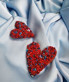 two red heart shaped brooches sitting on top of a blue satin material fabric