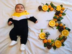 a baby laying on top of a white bed next to oranges and pine cones