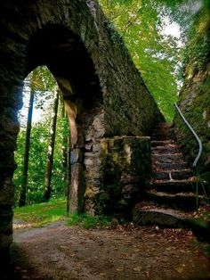 an old stone building with stairs leading up to it in the woods, surrounded by trees