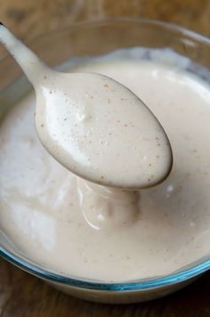 a spoon full of cream sitting in a glass bowl on top of a wooden table