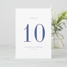 a table number card sitting on top of a white counter next to a vase with flowers