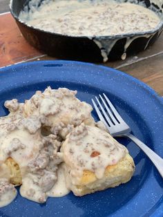 a blue plate topped with biscuits covered in gravy next to a skillet