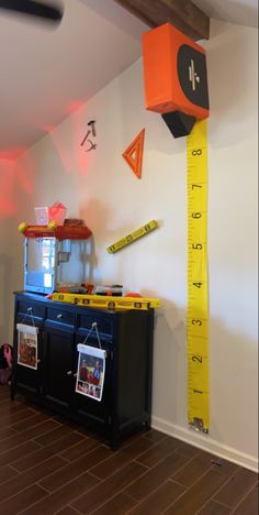 a room with a large ruler on the wall next to a black cabinet and yellow tape