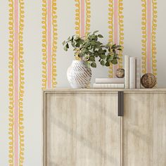 a white vase sitting on top of a wooden cabinet next to a wall with yellow and orange stripes