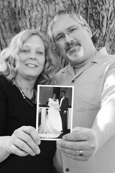 a man and woman pose for a photo in front of a tree with their wedding pictures