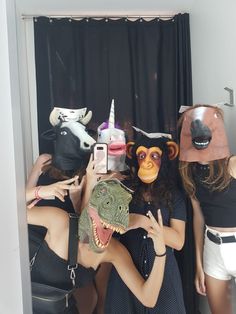 three women wearing animal masks are taking a selfie in front of a mirror with an alligator mask on