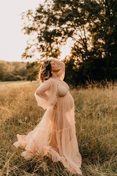 a pregnant woman in a dress standing in the middle of a grassy field at sunset