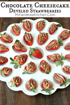 chocolate cheesecake deviled strawberries are arranged on a white platter with green leaves