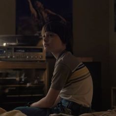 a young boy sitting on top of a bed in front of a tv set and sound equipment