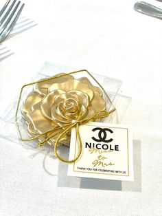 a table topped with a glass vase filled with gold flowers and a tag that says nicole