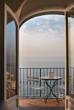 an open door leading to a balcony with table and chairs overlooking the ocean on a sunny day