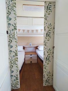 two twin beds in a small room with floral wallpaper on the walls and wood flooring