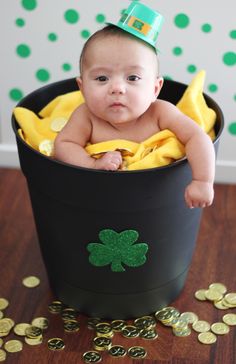 a baby is sitting in a pot full of gold coins and wearing a green hat