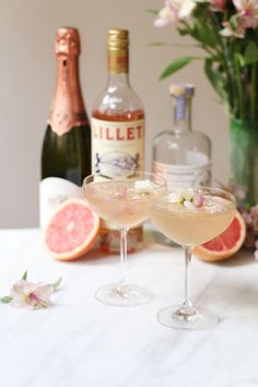 two wine glasses filled with champagne and garnished with flowers, next to bottles of gin