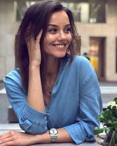 a woman sitting at a table with flowers in front of her and smiling for the camera