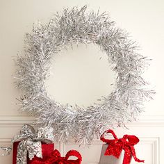 two wrapped presents sitting in front of a christmas wreath on a mantle with tinsel