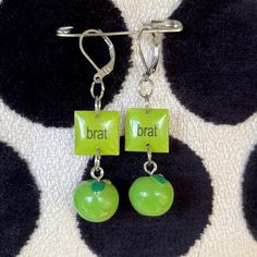 the earrings are green and have black dots on them with words that read bratt