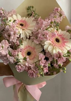 a bouquet of pink and white daisies in a paper wrapper with a bow