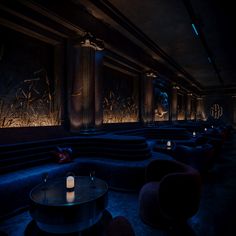 a dimly lit room with blue couches and candles on the tables in front of them