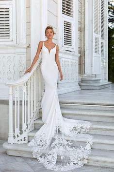 a woman in a white wedding dress standing on steps with her arms behind her back