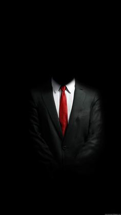 a man in a suit and red tie standing in the dark with his arms crossed