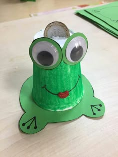 a green paper hat with googly eyes sitting on top of a table