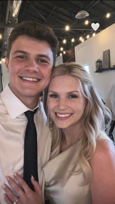 a young man and woman are posing for a photo in front of some string lights