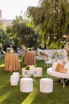 an outdoor wedding setup with white chairs and tables covered in gold cloths, surrounded by lush greenery