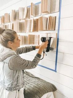 a woman is working on a wall mounted book shelf with a drill and some books