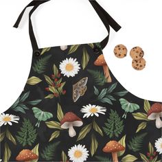 an apron with mushrooms, daisies and leaves on it is next to two cookies