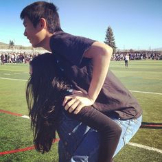 a man and woman hug on top of each other in front of a football field