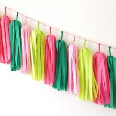 tissue tassels hanging from a line on a white wall with pink, green and yellow streamers