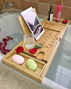 a bath tub with soaps, flowers and an electronic device on the tray next to it