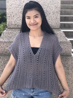 a woman standing in front of a stone pillar wearing a gray knitted sweater and jeans