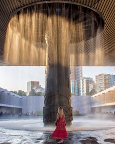 a woman in a red dress standing under a fountain with water pouring out of it