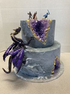 a three tiered cake with purple icing and dragon figurines on top