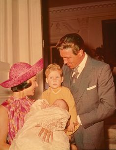 a man in a suit and tie holding a baby next to a woman wearing a pink hat