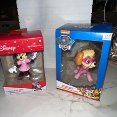 two toy figurines in boxes on a counter top, one is pink and the other is yellow