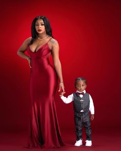 a woman in a red dress holding hands with a little boy wearing a tuxedo